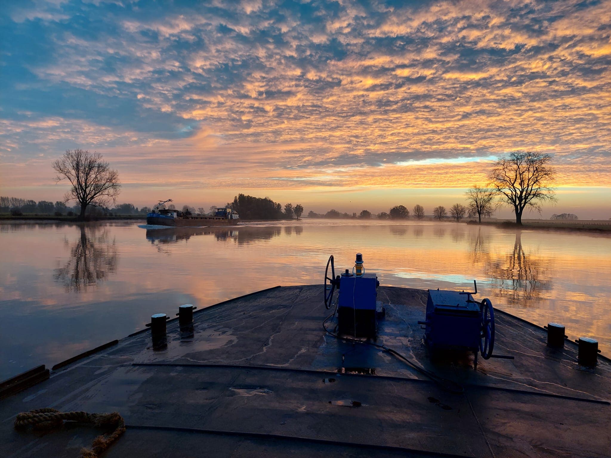 Zonsopgang over de rivier, gezien vanaf het dek van een binnenvaartschip
